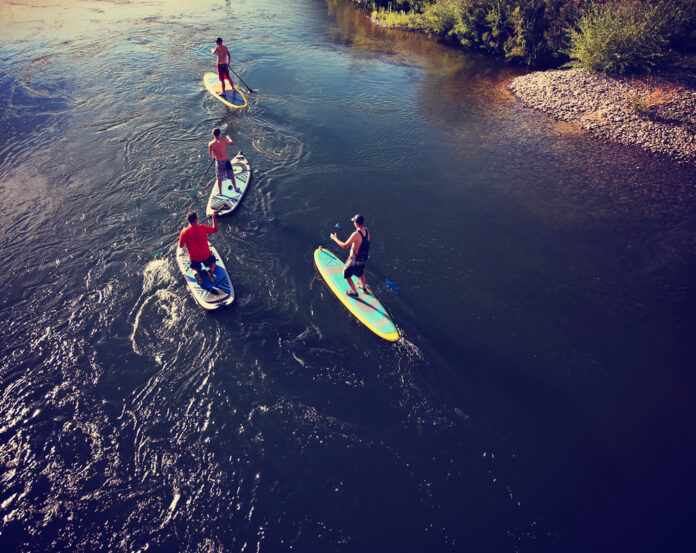 Unidentifiable,People,Paddle,Boarding,On,A,Calm,River,During,Summer